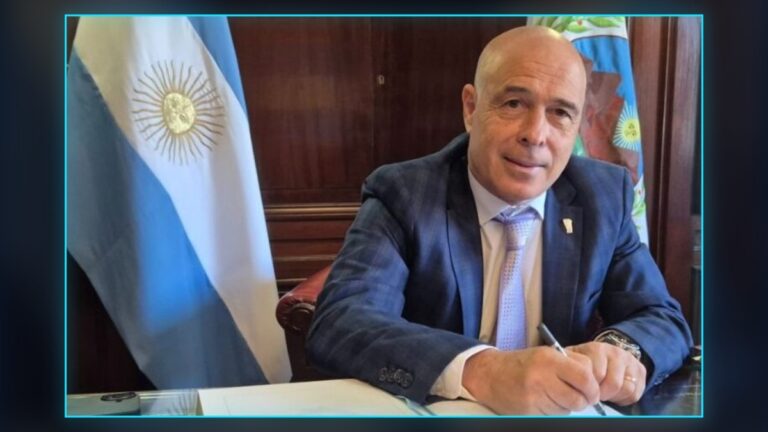 Funcionario firma documentos en un despacho junto a la bandera argentina